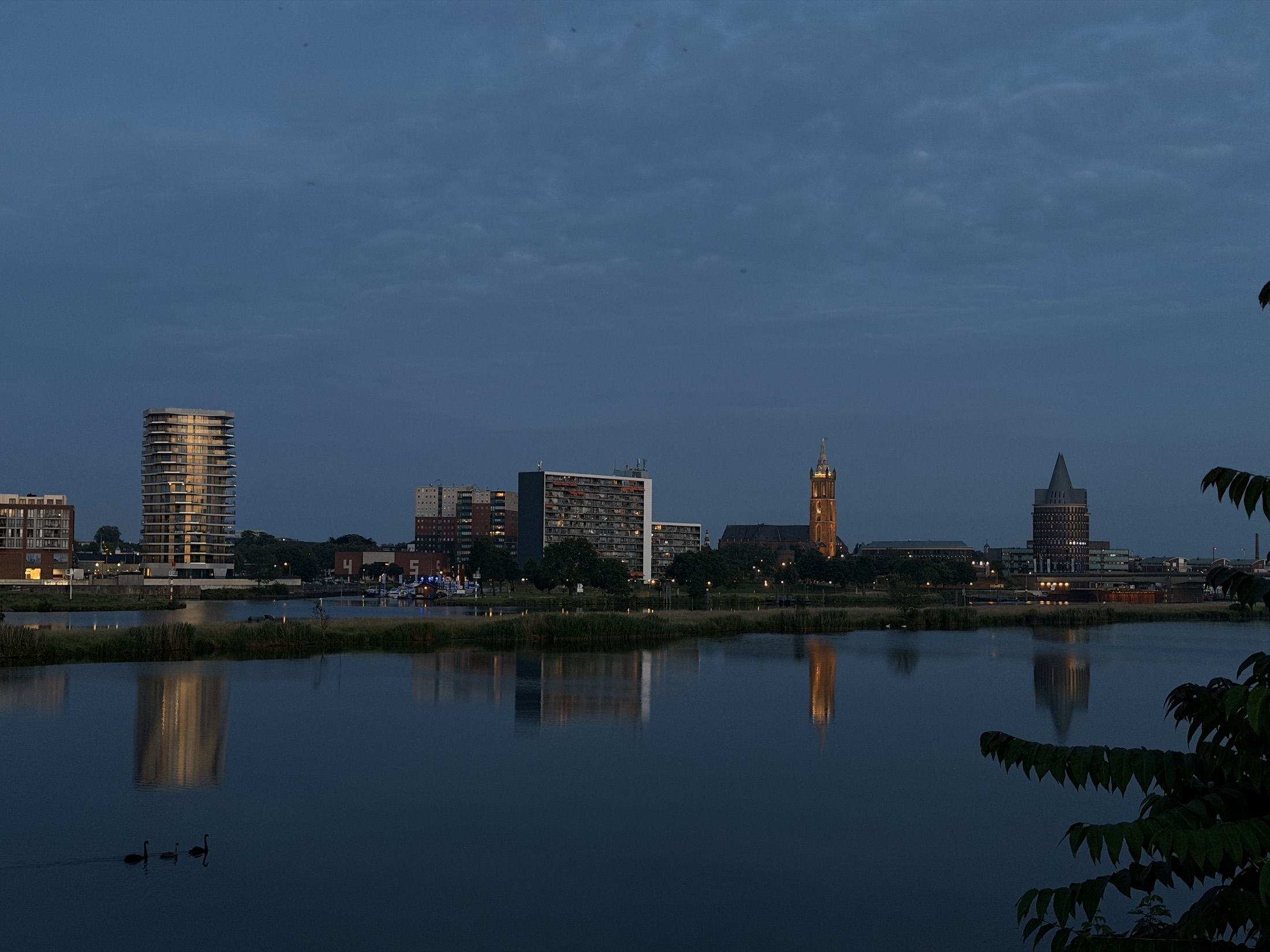 A city skyline at dusk reflected across the river beneath a blue evening sky